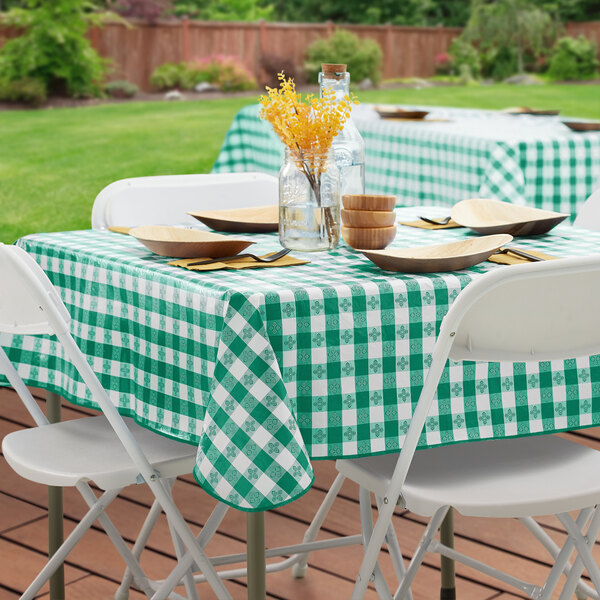 A green and white gingham vinyl table cover with a flannel back, draped over a rectangular table outdoors.