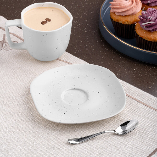 A plate with an Ariane Earth linen dots saucer and a cup of coffee with cupcakes on a table.