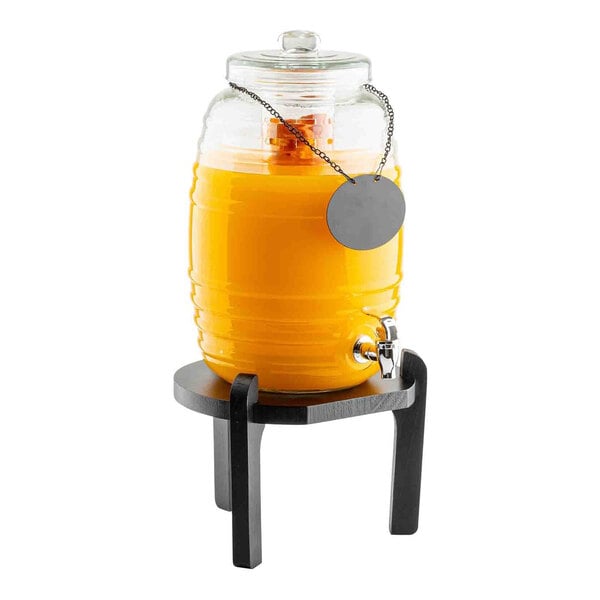 A black pinewood beverage dispenser stand holding a glass drink dispenser filled with orange liquid.