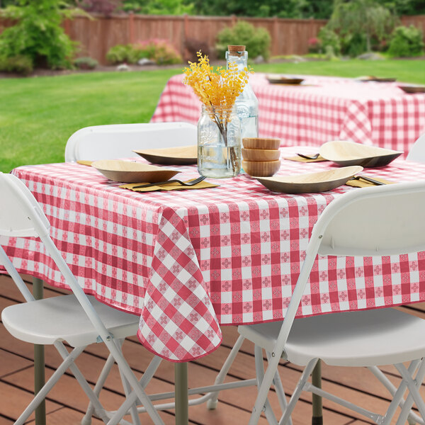 A rectangular table covered with a burgundy and white gingham vinyl tablecloth with a flannel back, set outdoors with folding chairs and simple tableware.