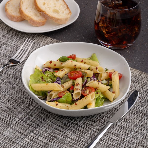A plate of pasta with vegetables and a salad on an Ariane porcelain plate on a table.