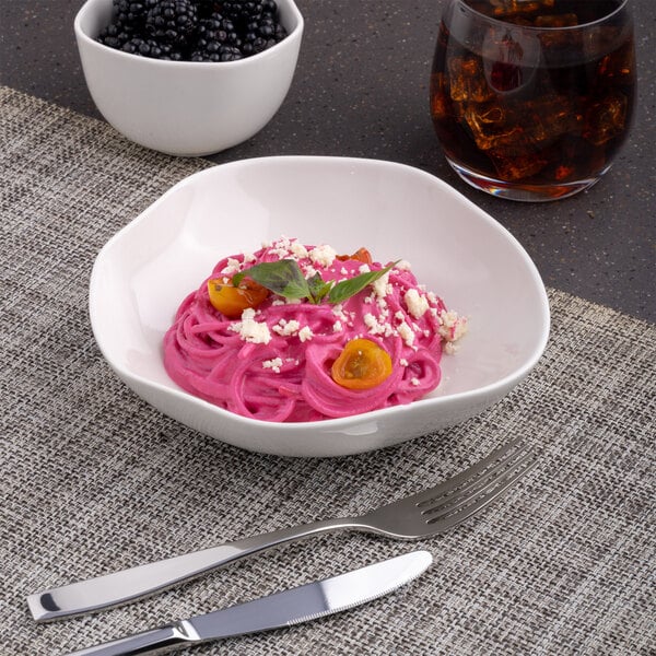 A warm white Ariane Earth porcelain bowl filled with pink pasta and blackberries.