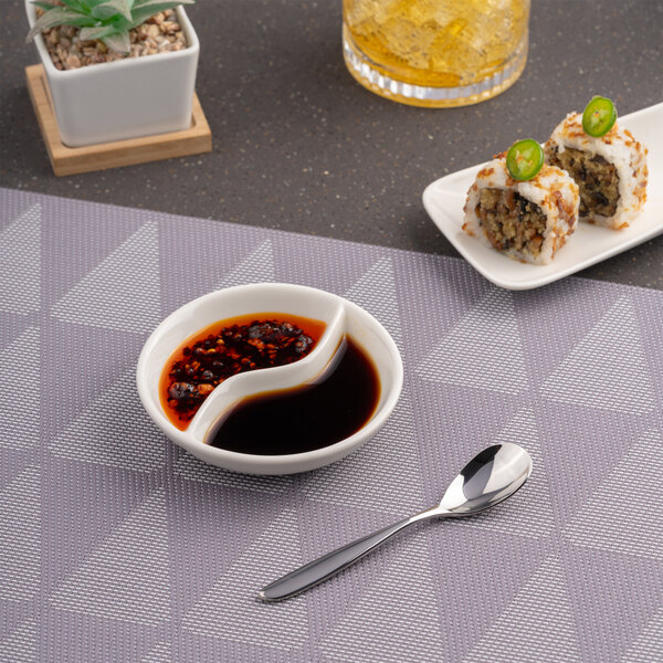 A round, warm white porcelain sauce dish with two divided compartments.