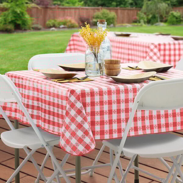 A rectangular red and white gingham vinyl table cover with a flannel back, draped over a table set outdoors.