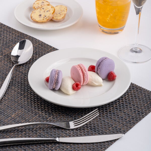 A round, warm white porcelain plate with a wide rim, shown holding colorful macarons and cream.
