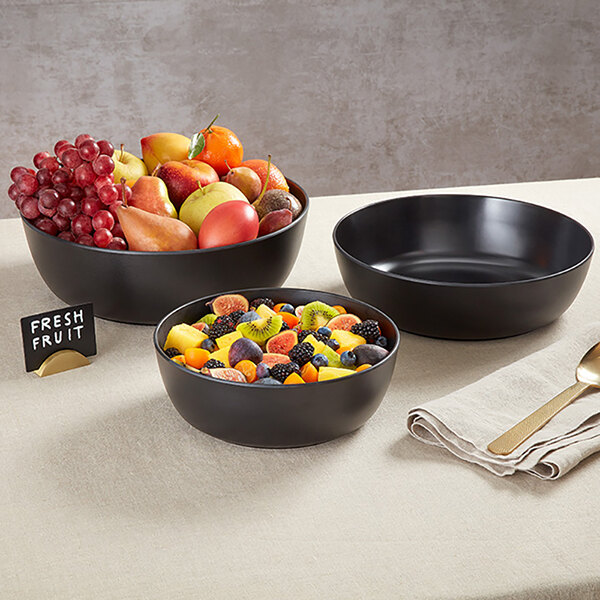 A large black round melamine serving bowl filled with assorted fresh fruit.