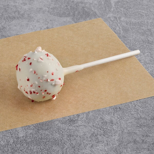 A peppermint candy cake pop coated in white chocolate with red and white candy pieces.