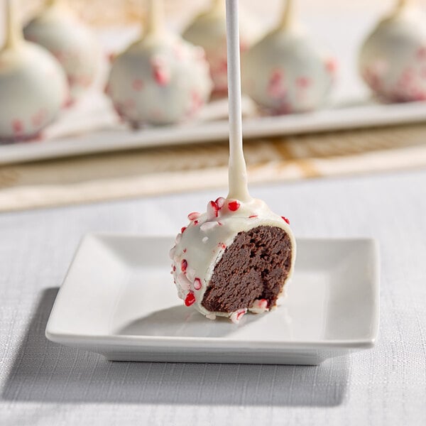 A chocolate cake pop coated in white chocolate and peppermint candy pieces, displayed on a small white plate.