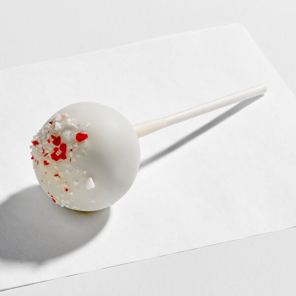 A white chocolate-coated cake pop with red and white peppermint candy sprinkles on a stick.