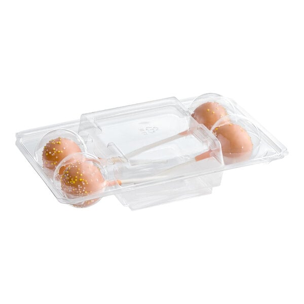 A clear plastic container holding four pumpkin cake pops with orange coating and yellow sprinkles.