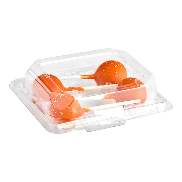 A clear plastic container holding three orange cake pops with white sprinkles.