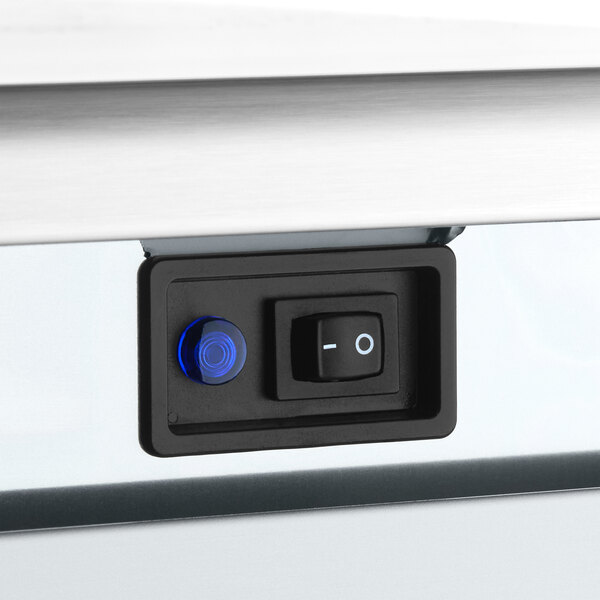 A close-up view of a control panel with a power switch and a blue indicator light on an undercounter ice machine.