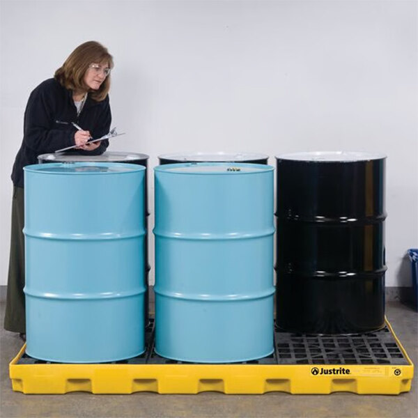 A yellow Justrite EcoPolyBlend 6-drum modular spill accumulation center holding four large industrial drums.