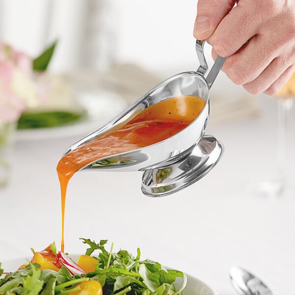 A stainless steel gravy boat being used to pour sauce onto a salad.