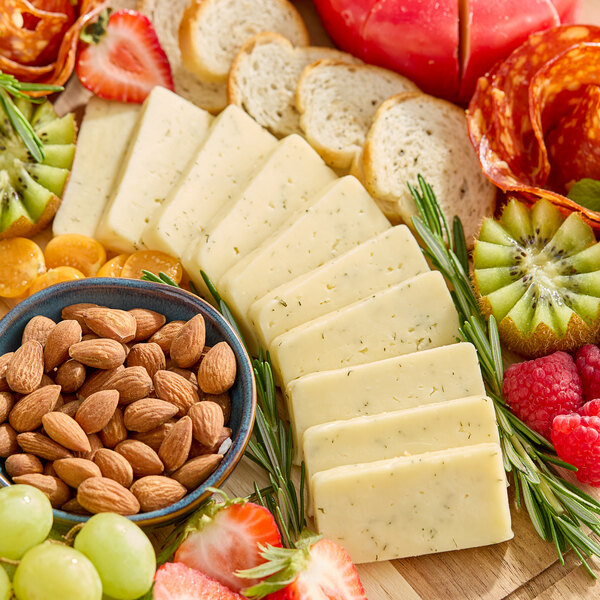 A block of Castello Dill Havarti cheese sliced and arranged on a charcuterie board with fruits, nuts, and bread.