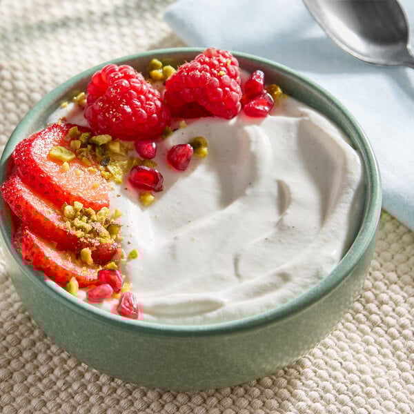 A bowl of dairy-free vanilla chamomile coconut yogurt alternative topped with strawberries, raspberries, pomegranate seeds, and chopped pistachios.