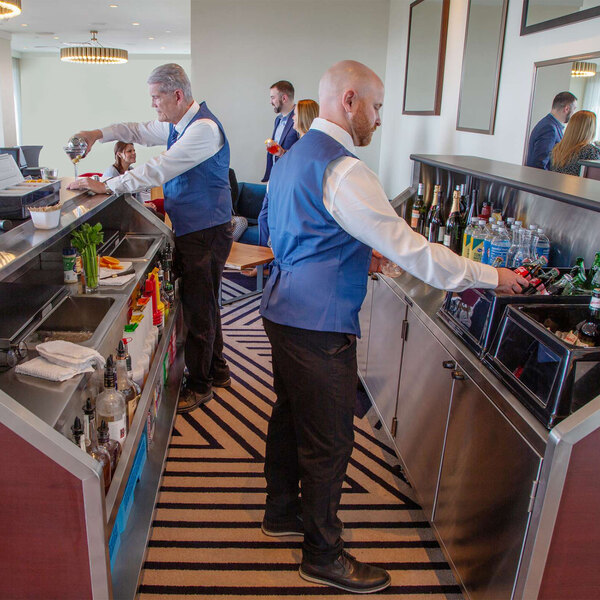 An 8-foot red maple laminate and stainless steel electric portable back bar with two locking storage compartments, shown in use by bartenders.