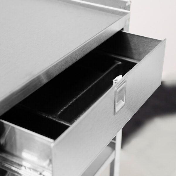 A stainless steel equipment stand with an open drawer and casters.
