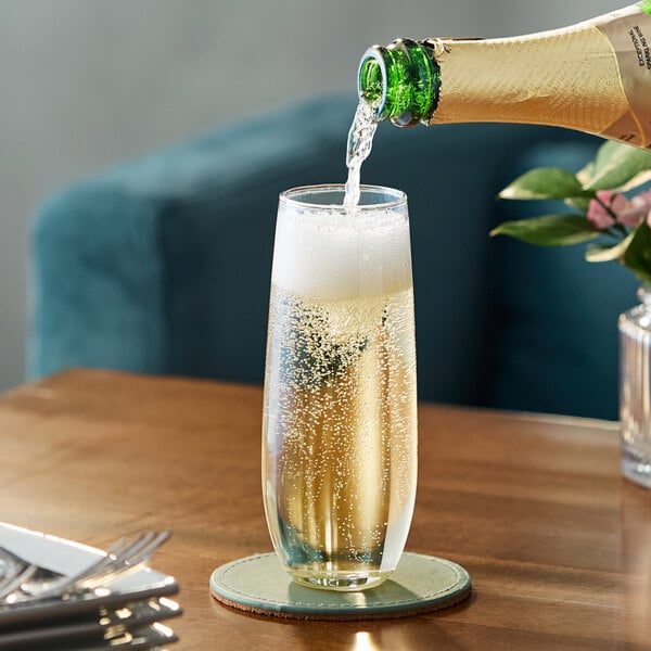 A stemless flute glass being filled with sparkling wine or champagne, placed on a coaster on a wooden table.