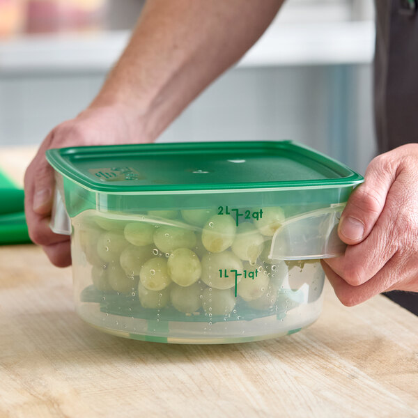 A translucent round plastic food storage container with a green lid, filled with grapes.