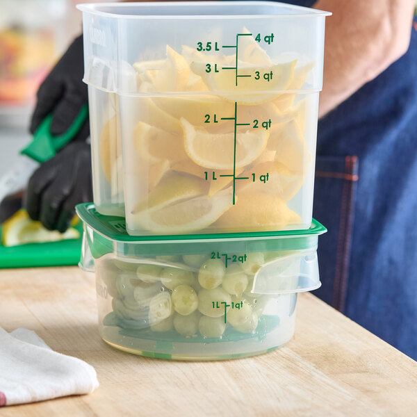 A translucent round polypropylene food storage container with green lid and measurement markings, filled with grapes.