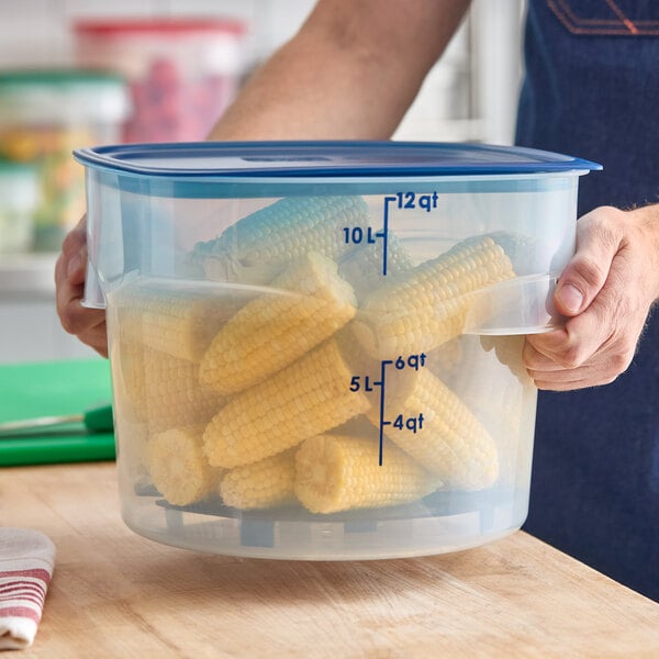 A large translucent round plastic food storage container with a blue lid, filled with corn on the cob and marked with quart and liter measurements on the side.