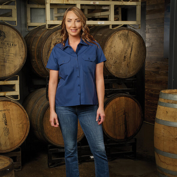 A women's navy blue short sleeve work shirt in XL size, modeled in front of wooden barrels.