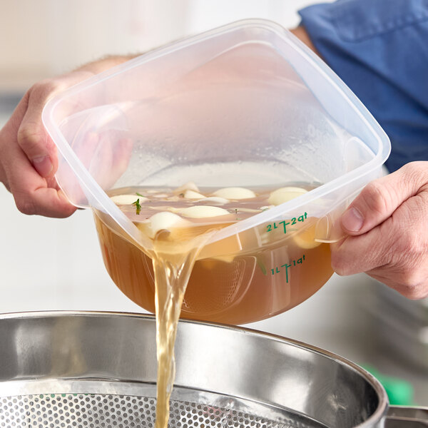 A translucent round polypropylene food storage container being used to pour liquid with ingredients into a strainer.