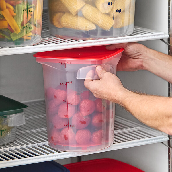 A translucent round polypropylene food storage container with a red lid, filled with strawberries and placed on a refrigerator shelf.