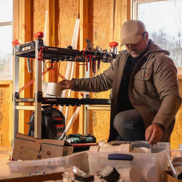 A foldable three-shelf jobsite cart with tools and supplies, used by a worker in a construction setting.