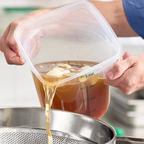 A translucent round 4-quart polypropylene food storage container being used to pour liquid through a strainer.
