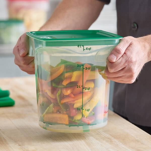 A translucent round 4-quart polypropylene food storage container with a green lid, filled with cut vegetables.