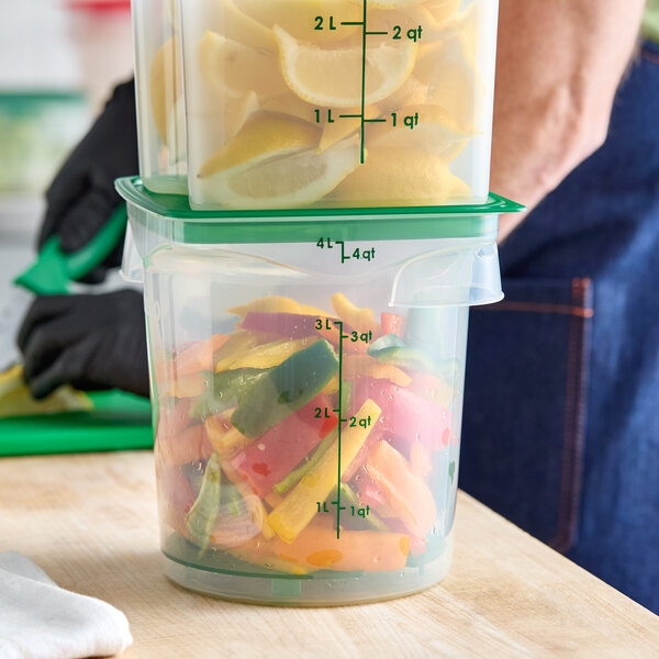 A translucent round polypropylene food storage container filled with cut vegetables and topped with another container holding lemon wedges.