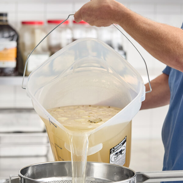 A translucent round food storage pail with a bail handle being used to pour liquid.