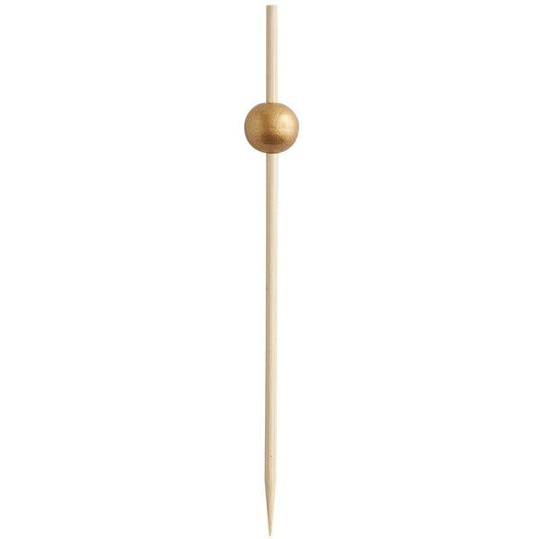 A bamboo cocktail pick with a gold ball decoration near the top.