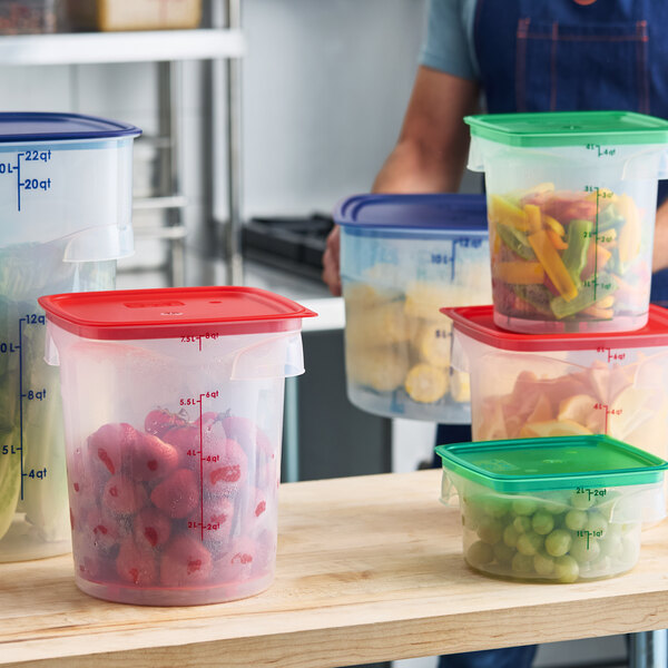 A translucent round polypropylene food storage container with a red lid, filled with strawberries and marked with measurement lines.
