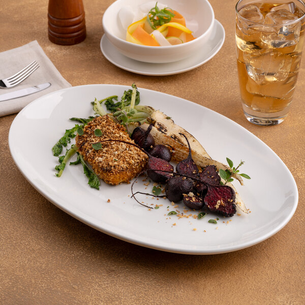 An oval, rimless, warm white porcelain coupe plate displayed on a table with food served on it.