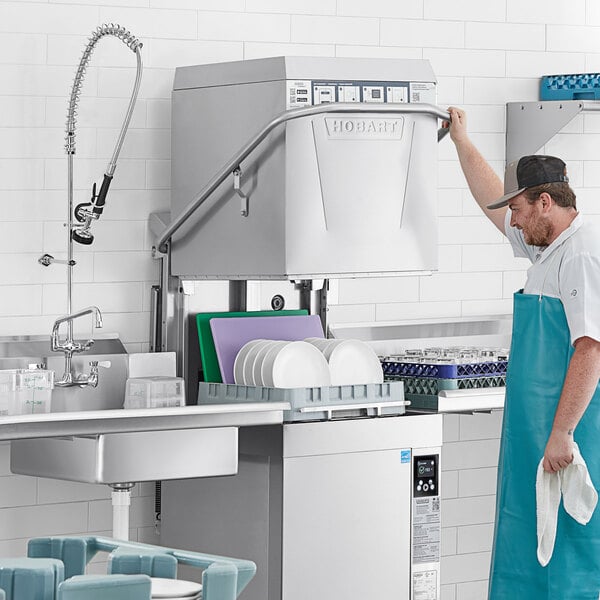 A commercial Hobart high temperature door-style ventless electric dishwasher with a booster heater, shown in a kitchen setting with a person operating it.