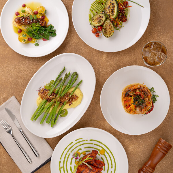 A set of oval white porcelain coupe plates displayed with various gourmet dishes.