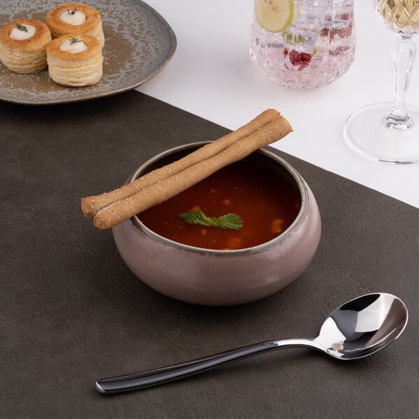 A round gold and brown porcelain bowl filled with soup, garnished with breadsticks and a mint leaf.