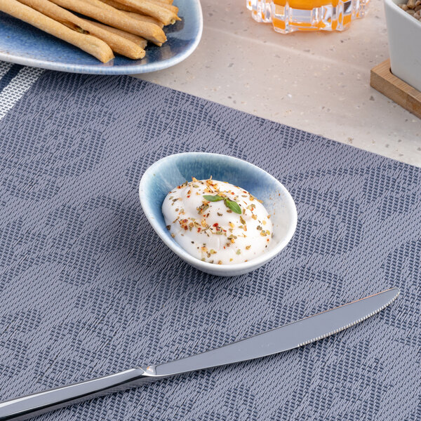 A small blue and white ombre slanted porcelain coupe bowl filled with a creamy dip and garnished with herbs and spices.