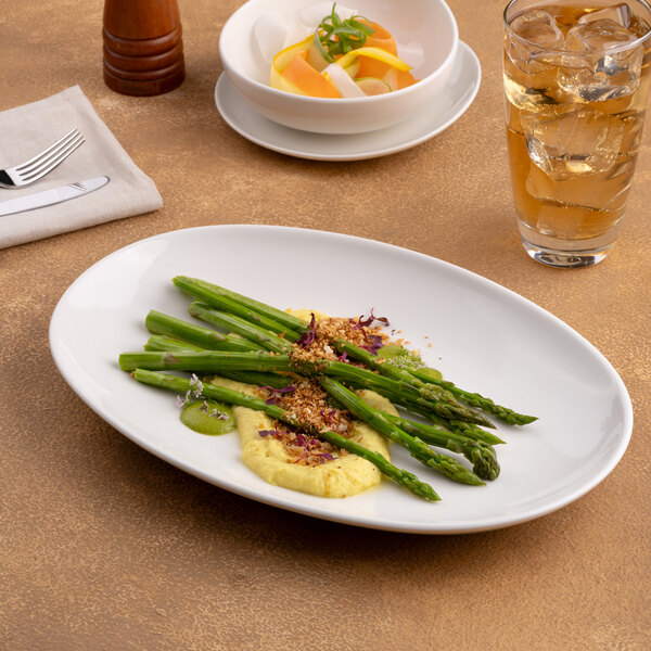 An oval, rimless warm white porcelain coupe plate displayed with food on a table.