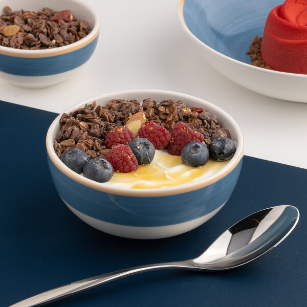 A blue and white two-tone round porcelain bowl filled with yogurt, granola, and berries.