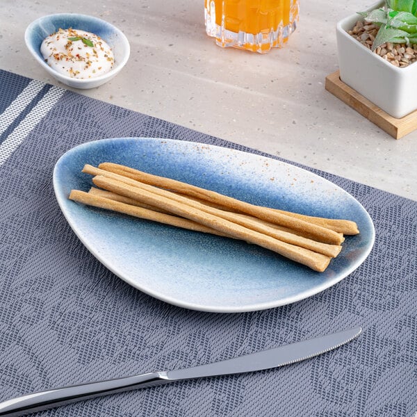 A blue and white ombre triangular porcelain coupe plate holding several breadsticks.