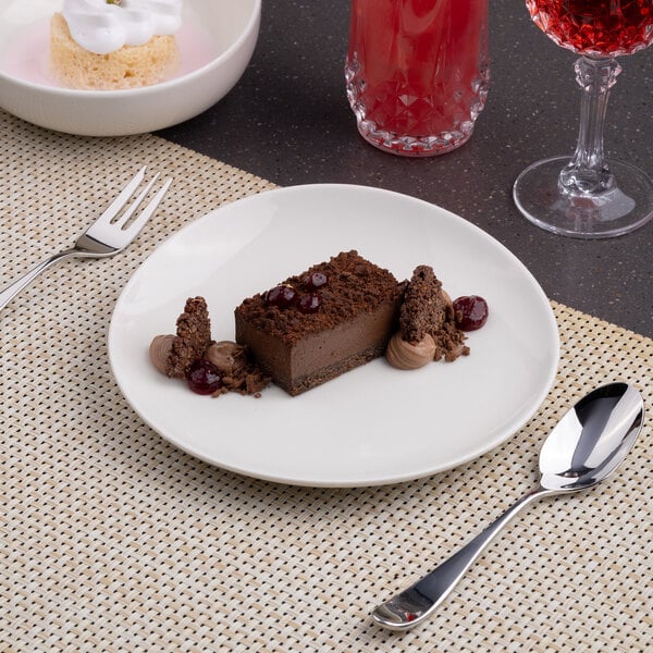 A round, warm white porcelain coupe plate with a slanted edge, shown holding a chocolate dessert.