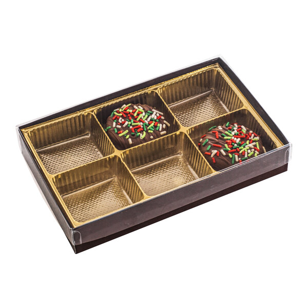 A rectangular brown and gold candy box with six cavities, two of which contain chocolate candies with colorful sprinkles, and a transparent lid.