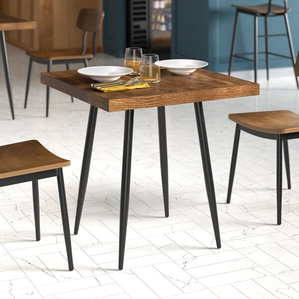 A square mid-century style dining table with a wooden top and black metal legs, set for two with plates, glasses, and utensils.