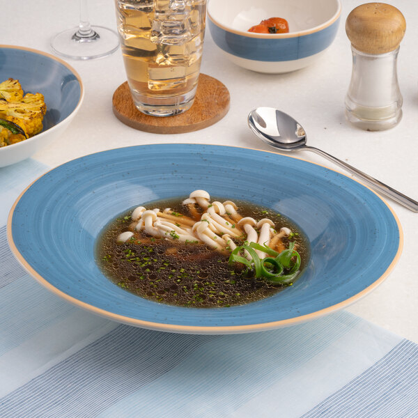 An oval blue porcelain bowl with a wide rim, filled with soup and garnished with mushrooms and green onions.