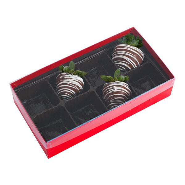 A rectangular red and black candy box with a transparent lid, containing three chocolate-covered strawberries in an eight-cavity tray.