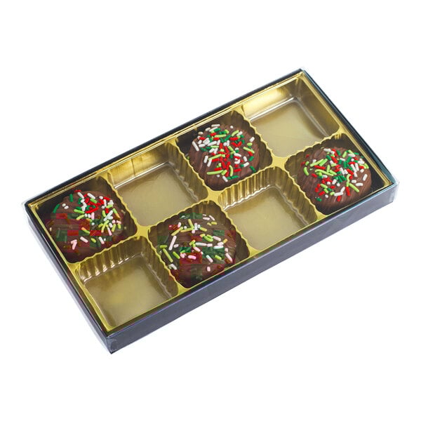 A rectangular brown and gold candy box with a transparent lid, containing four chocolate candies with colorful sprinkles in an eight-cavity tray.
